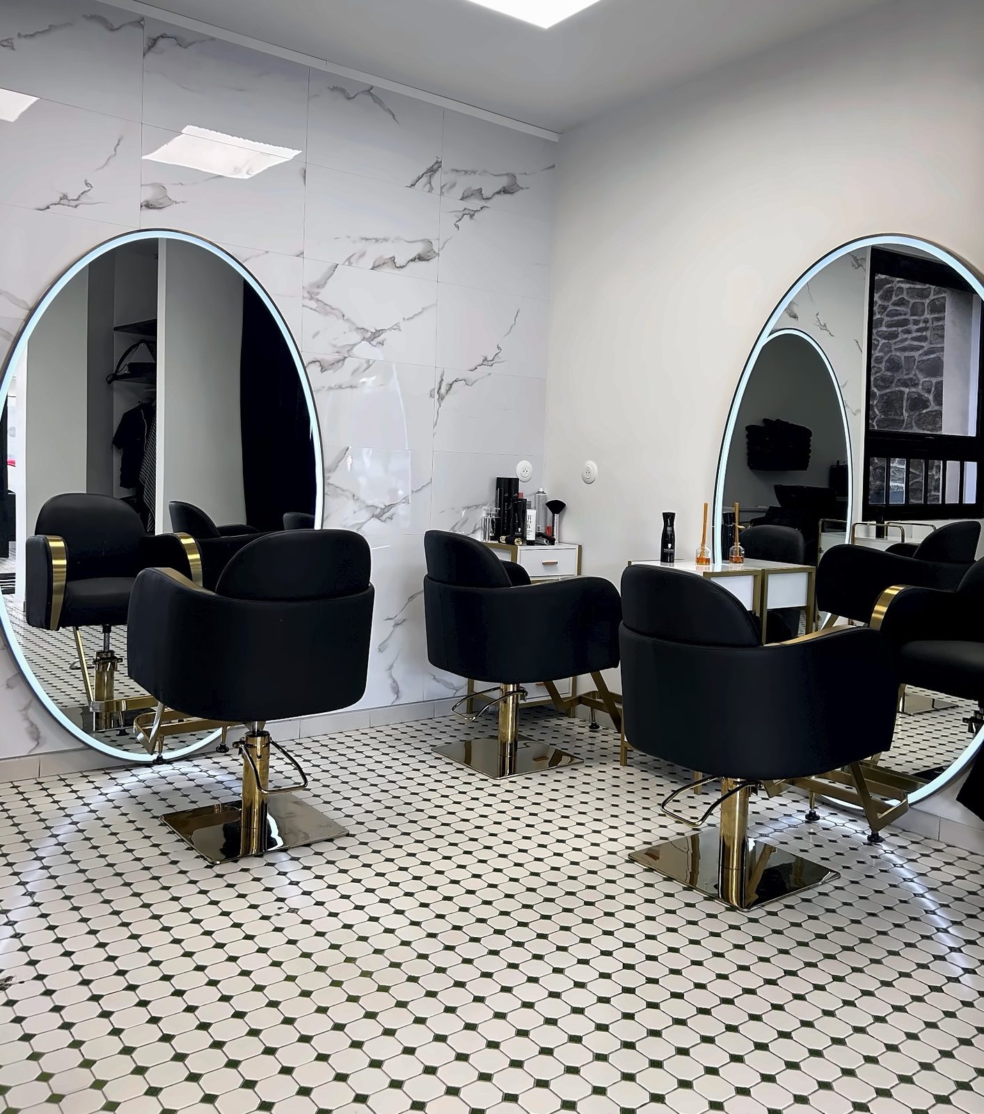 Postes de coiffage de Maison La Coiffeuse : miroirs ronds lumineux, fauteuils noir et or, mur en marbre
